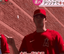 a baseball player wearing a red shirt with the letter a on it is standing in front of a wooden wall .