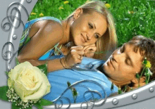 a man and a woman are laying in the grass with a white rose in the background .