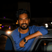 a man wearing a blue sweater and a watch leans on a car door