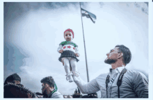 a man is holding a baby in his arms with a flag in the background