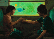 two children sitting in front of a window with a painting of planets on the wall