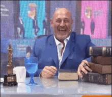 a man in a blue suit is sitting at a desk with a stack of books and a glass of water .