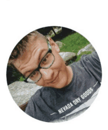 a young man wearing glasses and a nevada dry goods shirt takes a selfie