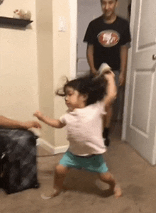 a little girl is dancing in a living room with a man in a san francisco 49ers shirt standing behind her .