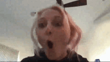 a woman is making a surprised face in front of a ceiling fan in a room .