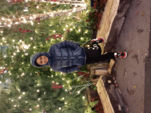 a young boy wearing a blue jacket and black pants is standing in front of a christmas tree