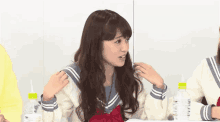 a girl in a school uniform sits at a table with bottles of water .