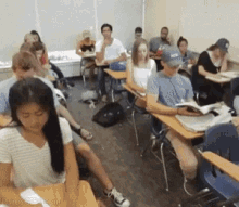 a group of students are sitting at their desks in a classroom with one wearing a hat that says nyc on it