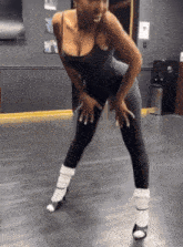 a woman in a black bodysuit and white socks is dancing on a black floor