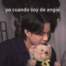 a young man is holding a teddy bear with the words yo cuando soy de angie written above him .