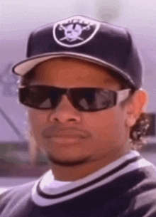 a man wearing sunglasses and a raiders hat looks at the camera .