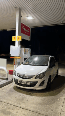 a white car with license plate ry04 sty is parked at a gas station