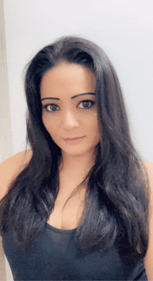 a woman with long black hair is wearing a black tank top and looking at the camera