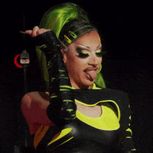 a woman with green hair is sticking her tongue out while wearing a black and yellow outfit