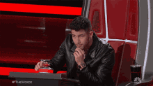 a man in a leather jacket is sitting in a chair with a nbc logo on the bottom