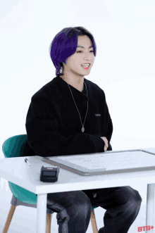 a young man with purple hair is sitting at a desk with the letters bts + on the bottom