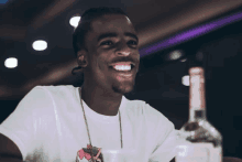 a man in a white t-shirt is smiling while holding a bottle of alcohol