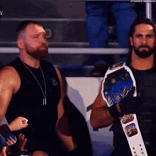 a couple of men standing next to each other in a stadium . one of the men is wearing a championship belt .