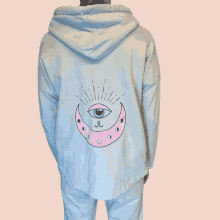 a person is wearing a light blue hoodie with a pink crescent moon and an eye on it