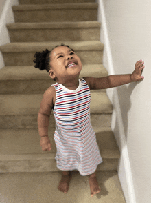 a little girl in a striped dress stands on the stairs