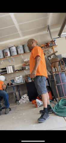 a man in an orange shirt and shorts is standing in a garage