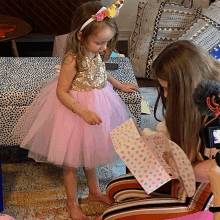 a little girl in a pink dress with a unicorn headband is standing next to another little girl