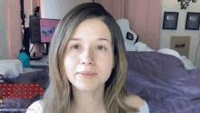 a woman without makeup is sitting in front of a bed and a computer monitor