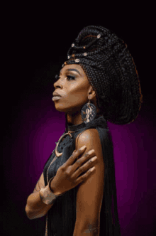 a woman wearing a braided headpiece and earrings stands with her hand on her chest