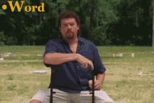 a man in a blue shirt is sitting on a chair in a field with the word word behind him