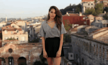 a woman in a gray top and black skirt stands in front of a cityscape