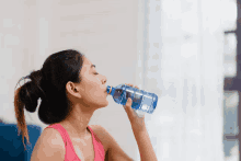 a woman drinking water from a blue bottle with a blue cap