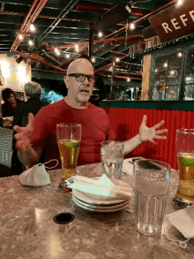 a man in a red shirt sits at a table in front of a sign that says " reef "