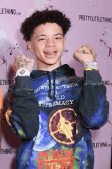 a young man wearing a tie dye hoodie and a watch is standing on a purple carpet .