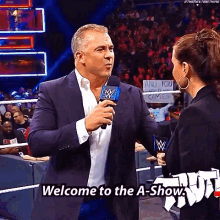 a man in a suit is talking into a microphone and says welcome to the a show