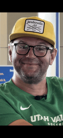 a man wearing a yellow hat and glasses is wearing a green utah valley shirt