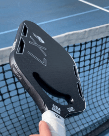 a person is holding a black luxe paddle on a tennis court