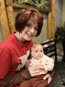 a woman holding a baby wearing a red shirt with a bear on it