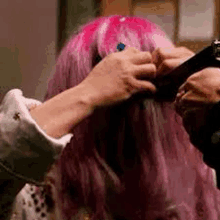 a woman with pink hair is getting her hair braided by another woman .