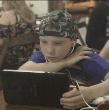 a young boy wearing a hat and ear buds is looking at a tablet