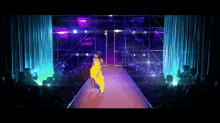 a woman in a yellow dress is walking down a runway in front of a crowd