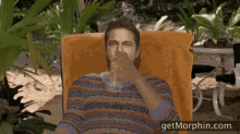 a man laying in a chair drinking orange juice with the website getmorphin.com visible