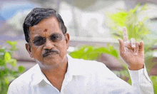 a man wearing glasses and a white shirt is making a funny face and pointing up with his finger .