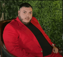 a man wearing a red suit and black shirt is sitting in a chair