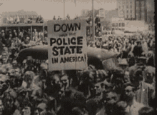 a black and white photo of a crowd holding a sign that says `` down police state in america '' .