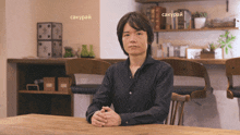 a man sits at a table with a sign that says sakurai on it