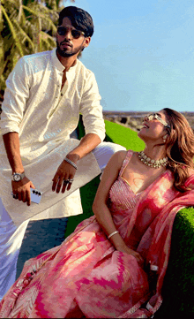 a woman in a pink dress sits next to a man in a white kurta