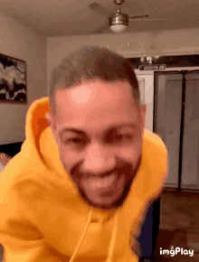 a man wearing a yellow hoodie is smiling in a room