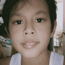 a close up of a young boy 's face with a white tank top on .