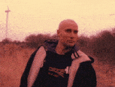 a man wearing a black shirt with a british flag on it stands in a field with a windmill in the background