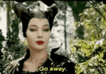 a woman in a black dress and horns is standing in the woods .